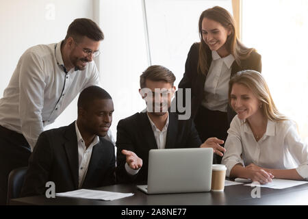 Smiling diverse employees cooperating in office using laptop Stock Photo
