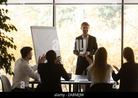 Excited diverse employees clap hands greeting male speaker Stock Photo