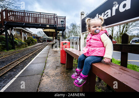 A little girl sits by the famous miniature ride along railway museum, popular with families and children, Staffordshire's tourist attraction Stock Photo