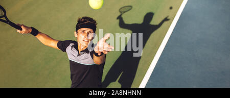 Top view of professional tennis player ready to hit the ball with the racket after tossing while serving in the beginning of a match. Stock Photo