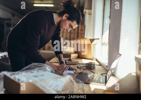 Man writing notes in the diary while standing at his workplace. Businessman making notes of the products ready for shipping in office. Stock Photo