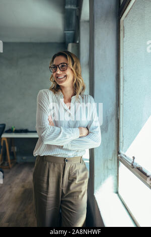 Businesswoman standing in office. Small business owner in casuals standing by window in office. Stock Photo