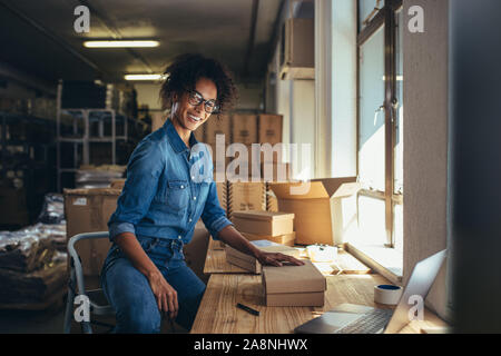 Smiling woman packing the parcel for shipping to the customer. Online business owner working at the office, preparing the order. Stock Photo