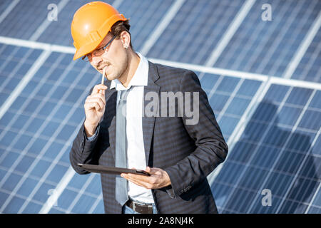 Businessman dressed in the suit with protective helmet working with digital tablet on a solar station. Concept of successful investment in alternative energy Stock Photo