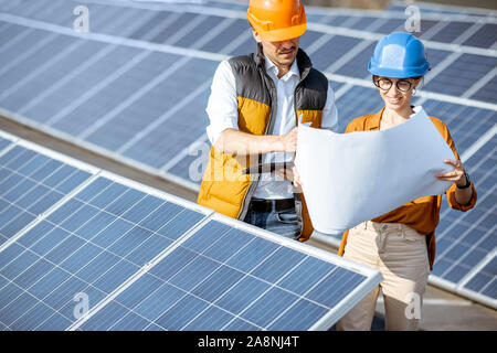 Two engineers or architects examining the construction of a solar power plant, standing with blueprints between rows of solar panels Stock Photo