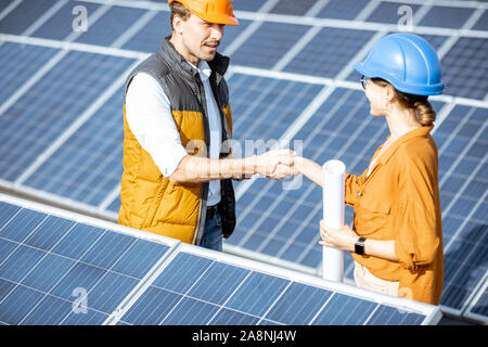 Two successful engineers or architects having a deal, shaking hands while standing between rows of solar panels on a photovoltaic power plant Stock Photo