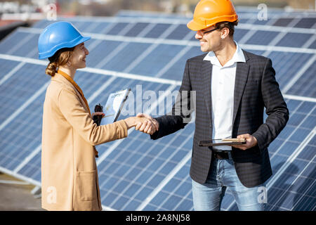 Business man and woman dressed in the suits having a deal, shaking hands while standing on a solar power station Stock Photo