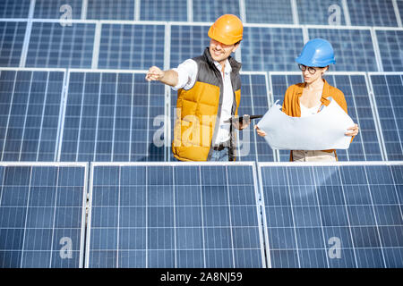 Two engineers or architects examining the construction of a solar power plant, standing with blueprints between rows of solar panels Stock Photo
