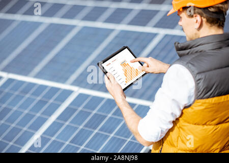 Man examining genaration of solar power plant, holding digital tablet with a chart of electricity production. Concept of online monitoring of the electric station Stock Photo