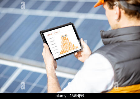 Man examining genaration of solar power plant, holding digital tablet with a chart of electricity production. Concept of online monitoring of the electric station Stock Photo