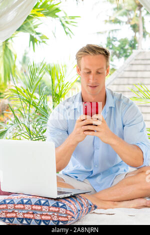 Attractive man using smartphone with palms on the background Stock Photo