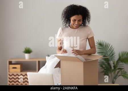 Smiling African American woman unpacking parcel, removing bubble wrap Stock Photo