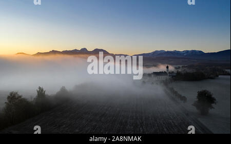 Beautiful foggy autumn morning in Bavaria - aerial view of Wilparting Church before Alps in Chiemgau Stock Photo