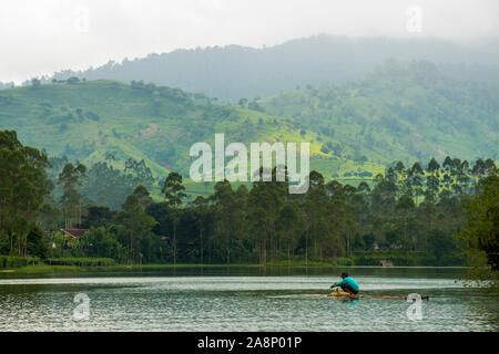 Indonesian Fisherman on bamboo raft with hill in the background, at Cileunca Lake, Pangalengan, Bandung, West Java, Indonesia Stock Photo