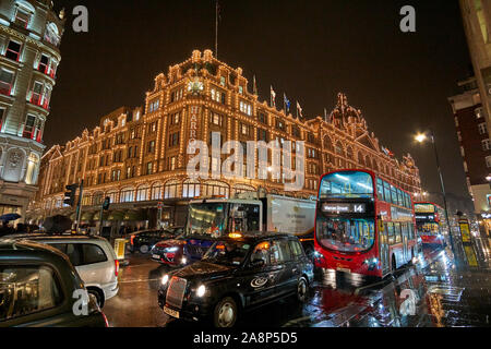 Exterior view of Harrods Department Store in London at night during Winter period. Night traffic street scenery in a typical rainy day. Stock Photo