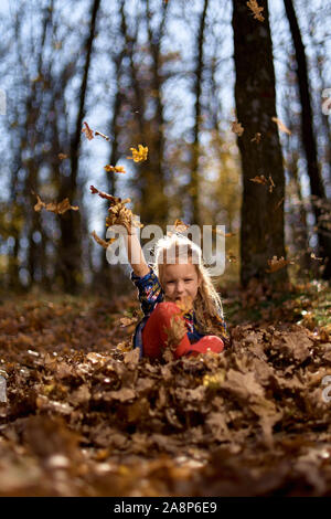 Amazing leaf. Cute girl in a big pile of foliage. Small girl smile sitting on fall leaves. Little child girl enjoy playing on fresh air. Stock Photo