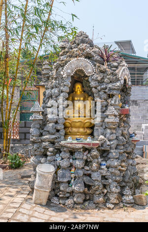 Nha Trang, Vietnam - March 11, 2019: Chua Loc Tho Buddhist temple, primary school and orphanage. Golden statue of smiling Buddha in grotto under green Stock Photo