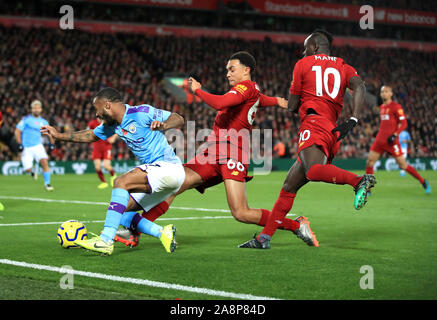 Manchester City's Raheem Sterling (left) goes down under pressure from Liverpool's Trent Alexander-Arnold and Sadio Mane (right) during the Premier League match at Anfield, Liverpool. Stock Photo