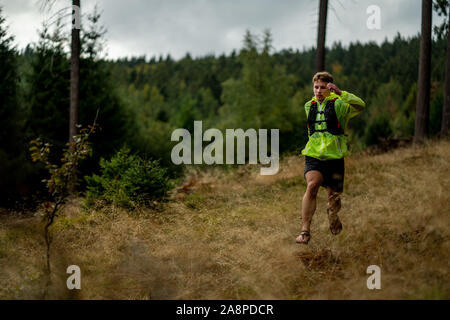 A young athlete in barefoot shoes runs down the mountain. Mountain run. Cross Country Running. Individual sports Stock Photo