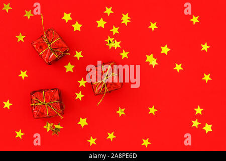 Three red gift boxes on a red background with golden stars. Festive flat lay for Christmas and New Year greeting card. Top view. Stock Photo