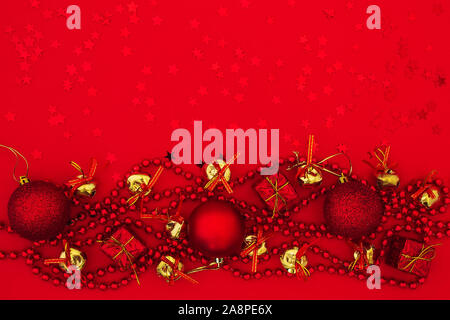 Christmas balls, gift boxes, golden bells with bows and bead garland on a red background with red stars. Festive flat lay for Christmas and New Year. Stock Photo