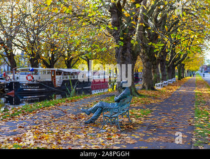 Grand Canal Dublin, sculpture, Patrick Kavanagh, poet, on seat. Canal waters, barges and towpath. Fall / autumn season with colorful leaves. Ireland Stock Photo