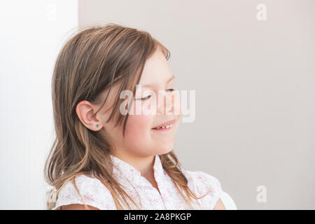 Smiling funny blond Caucasian little girl, close-up portrait with closed eyes over gray wall background Stock Photo