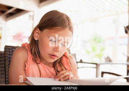 Little blond Caucasian girl reads a menu in a restaurant, close up photo with sleletive focus Stock Photo