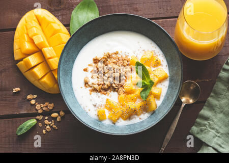 Yogurt bowl with mango and breakfast cereals oat granola on a wooden table. Top view. Toned image. Concept of dieting, weight loss, healthy eating and Stock Photo