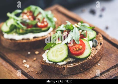 Rye bread with cream cheese and cucumber toast garnished with cherry tomato, arugula leaf and seeds. Healthy snack, clean eating. Closeup view, select Stock Photo