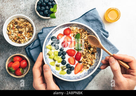 Yogurt bowl with fresh fruits, berries and granola. Vegetarian food, clean eating concept. Male hands holding superfood yogurt smoothie bowl Stock Photo