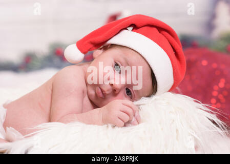 Little baby girl in red Santa hat is wondering what will be a Christmas. Christmas concept. Stock Photo