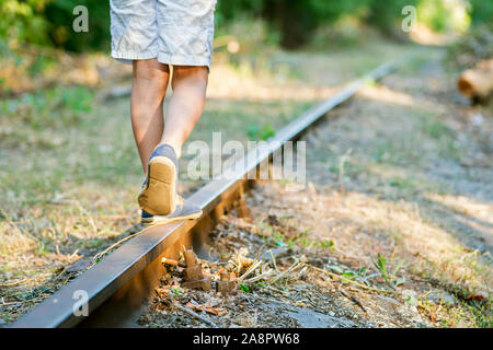 Little boy steps on the rails of the railway, being exposed to danger. Young boy balancing on a train rail. Stock Photo