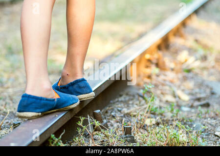 Little boy steps on the rails of the railway, being exposed to danger. Young boy balancing on a train rail. Stock Photo