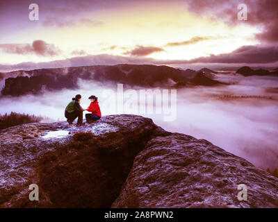 Night photo A woman shows magical lightning lantern to her man.  Woman sits on a rock and shines to misty darkness.  First Sun rays appear in the clou Stock Photo