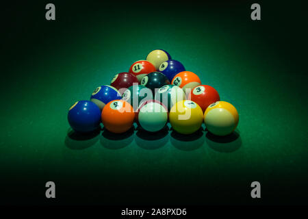 Colorful numbered balls with their shades are forming triangle on green table. Horizontal background with equipment for American billiard cue sport ga Stock Photo