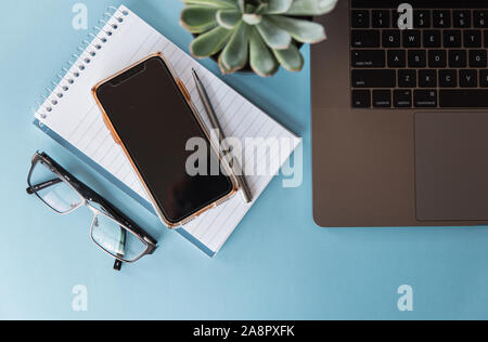 Overhead view of workspace with laptop, phone, glasses and notepad. Stock Photo