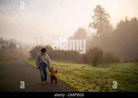 A mother and her baby walk on a paved path in the dense morning fog.