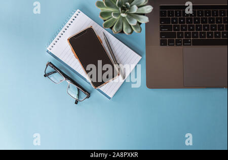 Overhead view of workspace with laptop, phone, glasses and notepad. Stock Photo