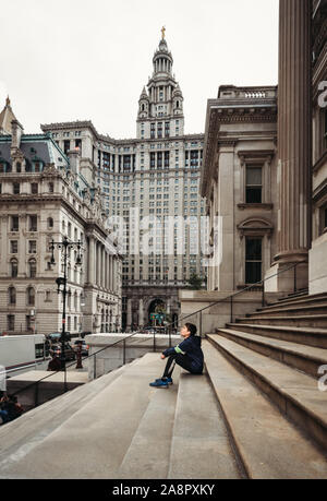 Boy sitting on stone steps surrounded by buildings in New York City. Stock Photo