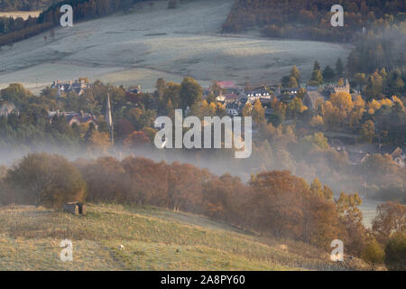 A Misty View of Braemar from the Lower Slopes of Morrone in Autumn, with Braemar & St Margaret's Churches Visible Above the Trees. Stock Photo