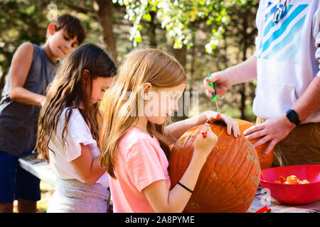 Three Young Children Carving Pumpkins Outdoors Stock Photo