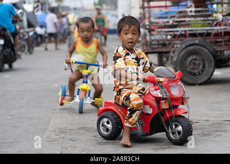 Two young Filipino boys playing in a poor area of Cebu City riding toy tricycles. Stock Photo