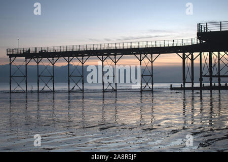 Bognor Regis historic Pier with a beautiful sunset behind and reflections on the sand at low tide. Stock Photo