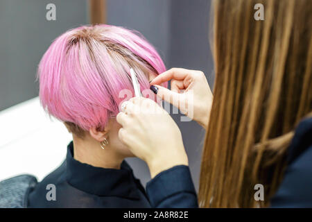 Hands Of Hairdresser Checks Short Pink Hair Of Girl On Gray