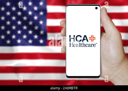 Logo of public company HCA Healthcare displayed on a smartphone. Flag of USA background. Credit: PIXDUCE Stock Photo