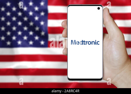 Logo of public company Medtronic plc displayed on a smartphone. Flag of USA background. Credit: PIXDUCE Stock Photo