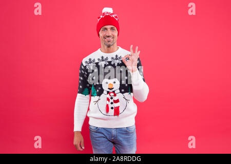 For seasonal comfort. Happy man give OK sign in fashion snowman jumper. Cold weather male style and fashion. Winter mens fashion trends. Keep in warmth with eye-catching fashion design. Stock Photo