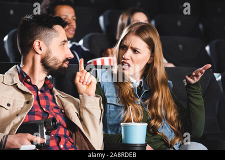 selective focus of man shooting with digital camera and showing shh gesture to angry woman in cinema Stock Photo