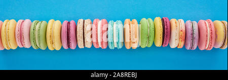 panoramic shot of multicolored delicious French macaroons in row on blue bright background Stock Photo